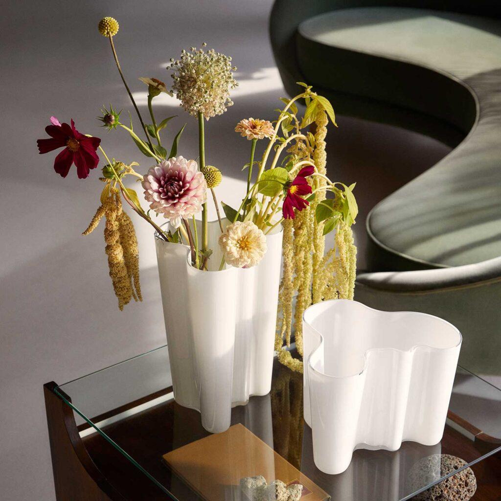 Frühlingsdeko: So atmet Ihr Zuhause wieder auf 1 Weiße Iittala Aalto Vasen in zwei verschiedenen Höhen auf einem Glas-Couchtisch neben deinem grünen Sofa.