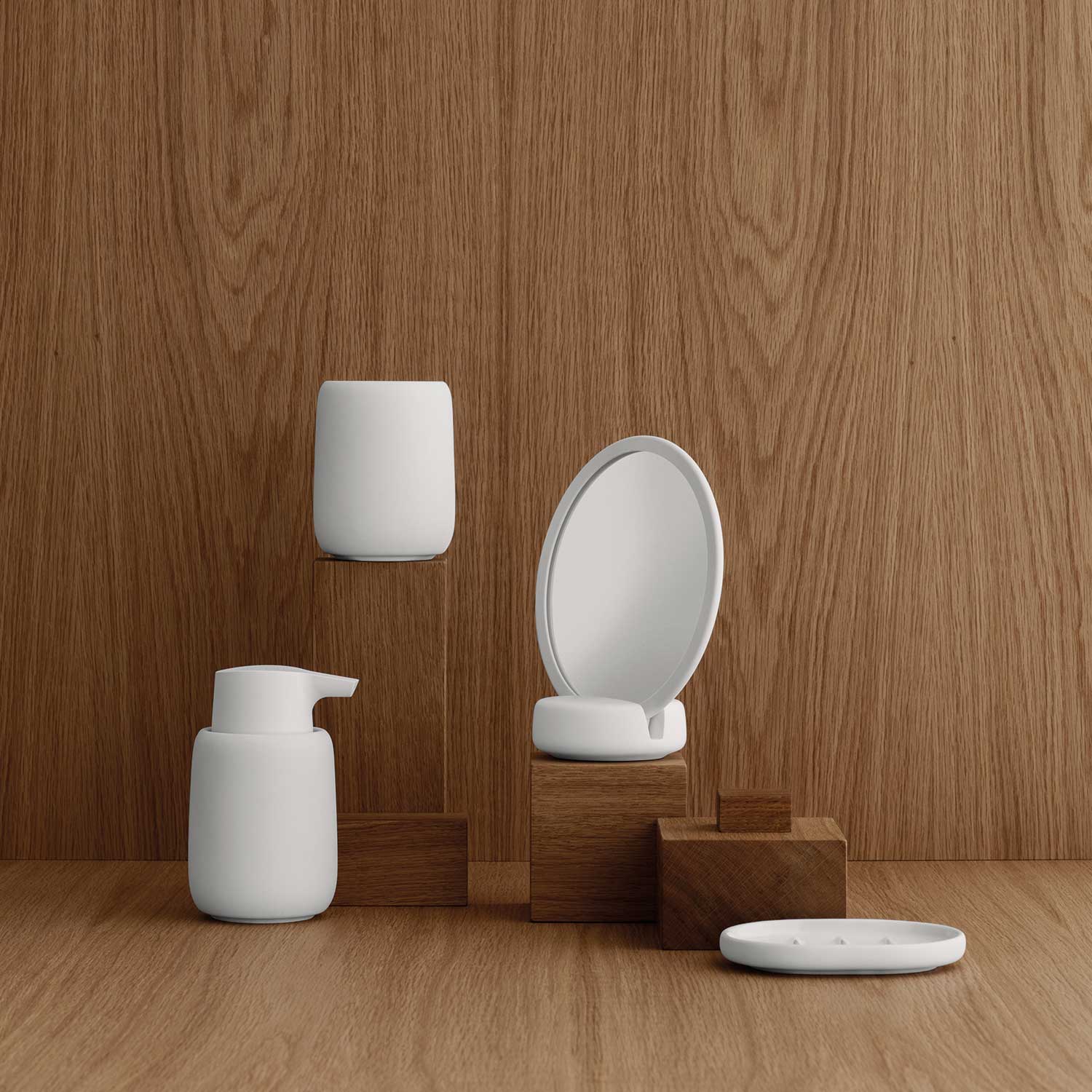 Weiße blomus – Sono Bad-Accessoires mit Seifenspender, Kosmetikspiegel und Tablett vor Holzwand