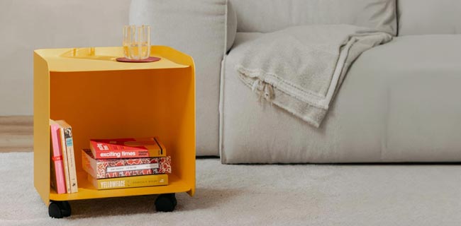 Metallbude Juno Rollcontainer in orange vor einem Sofa