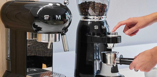SMEG Kaffeevollautomat Kaffeemühle in schwarz neben Kaffeemaschine